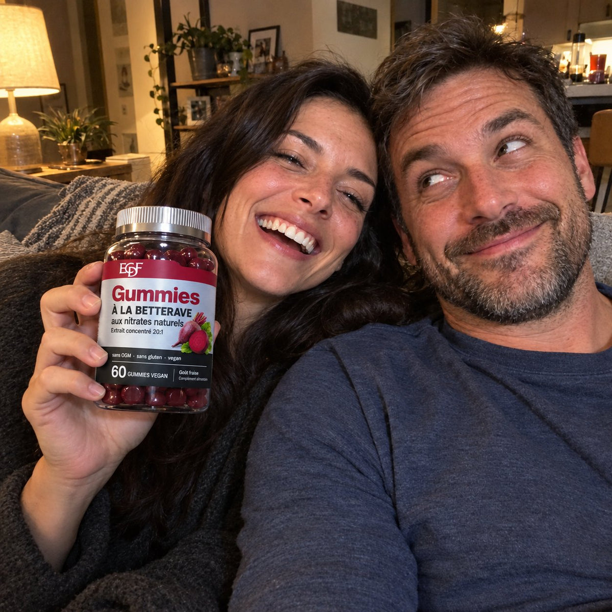 Un couple rit sur le canapé, elle tient le pot de gummies à la betterave