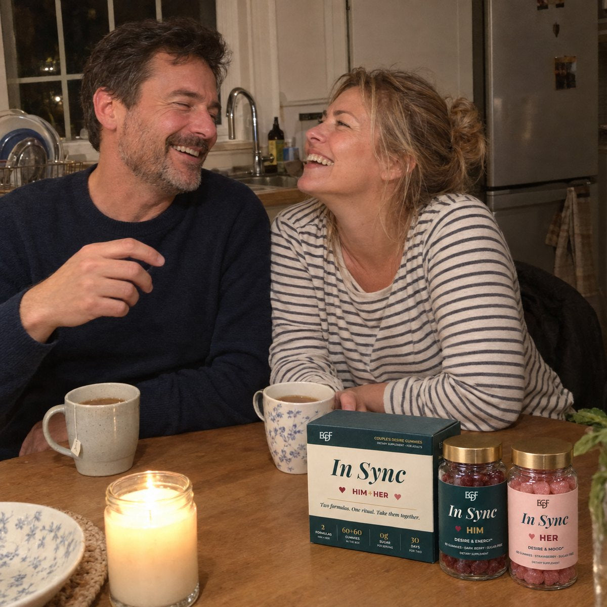 Un couple rit à la table de la cuisine le soir, avec du thé, une bougie et le coffret In Sync